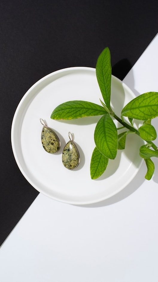 Coleção Folhas espalhada sobre tecido bege: brincos verdes de formatos diferentes, entre folhas de verdade, mostrando o desenho inspirado na natureza e o acabamento artesanal.